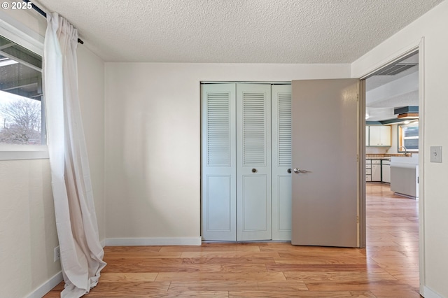 unfurnished bedroom featuring light wood-type flooring, a textured ceiling, and a closet