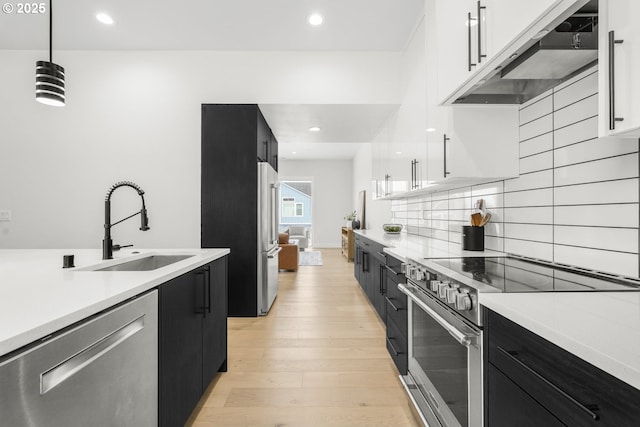 kitchen with sink, premium appliances, extractor fan, white cabinets, and decorative light fixtures