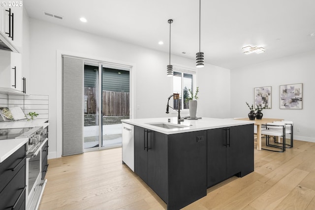 kitchen with pendant lighting, sink, appliances with stainless steel finishes, a kitchen island with sink, and light hardwood / wood-style floors