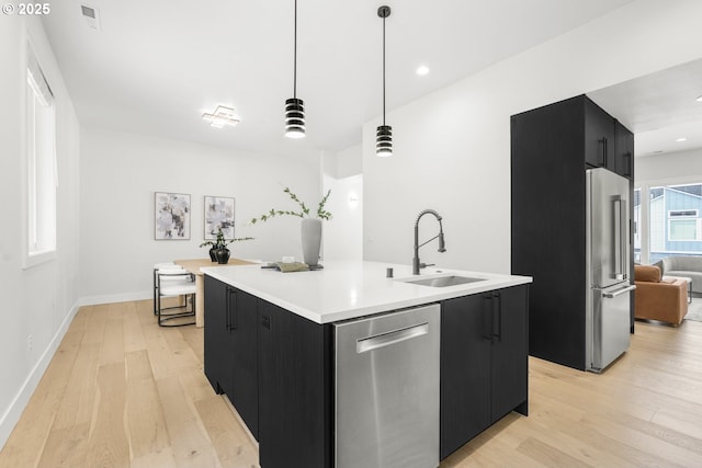 kitchen with sink, decorative light fixtures, a center island with sink, appliances with stainless steel finishes, and light hardwood / wood-style floors