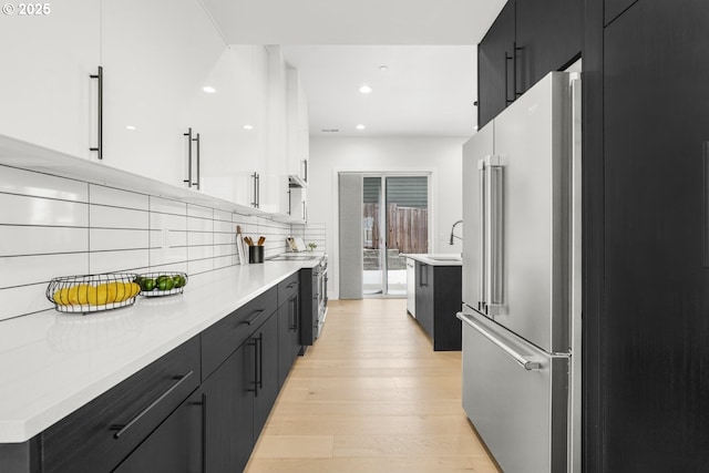 kitchen featuring appliances with stainless steel finishes, tasteful backsplash, sink, white cabinets, and light wood-type flooring