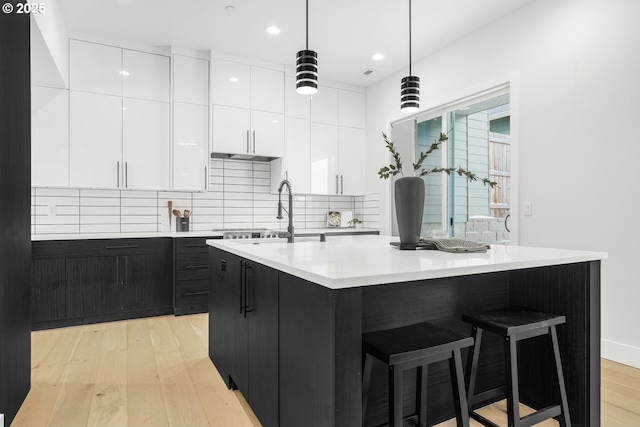 kitchen with a kitchen island with sink, pendant lighting, white cabinets, and backsplash