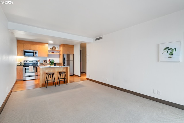 kitchen featuring a center island, a breakfast bar area, light carpet, appliances with stainless steel finishes, and light brown cabinetry