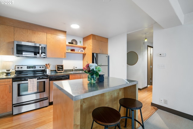 kitchen with appliances with stainless steel finishes, sink, a center island, light wood-type flooring, and a kitchen breakfast bar