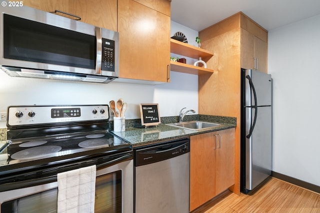 kitchen featuring sink, dark stone countertops, stainless steel appliances, and light hardwood / wood-style flooring