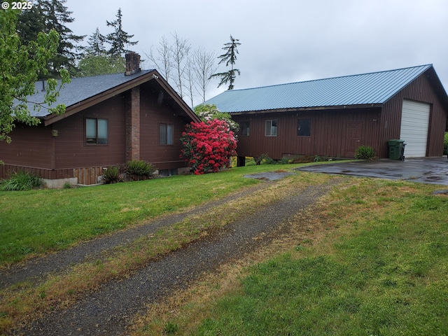 view of side of property featuring driveway, a chimney, a garage, a lawn, and metal roof