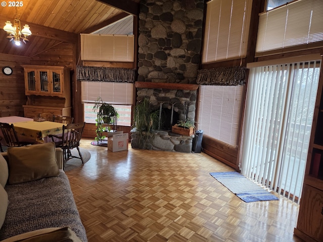 living room featuring a chandelier, wood walls, beam ceiling, a stone fireplace, and high vaulted ceiling