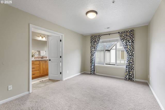 unfurnished bedroom with ensuite bath, light carpet, and a textured ceiling