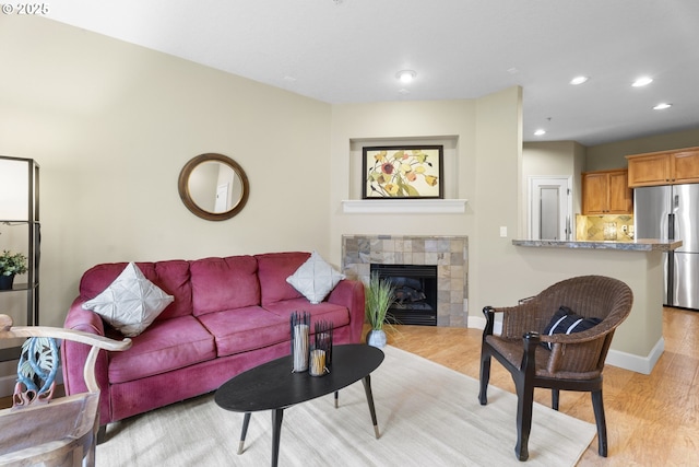 living room with a tiled fireplace and light wood-type flooring