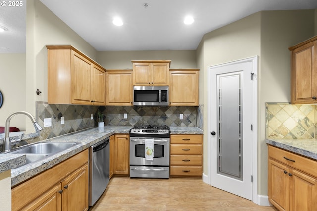 kitchen with stainless steel appliances, sink, light hardwood / wood-style flooring, and backsplash