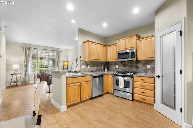 kitchen featuring sink, light stone counters, light wood-type flooring, appliances with stainless steel finishes, and kitchen peninsula