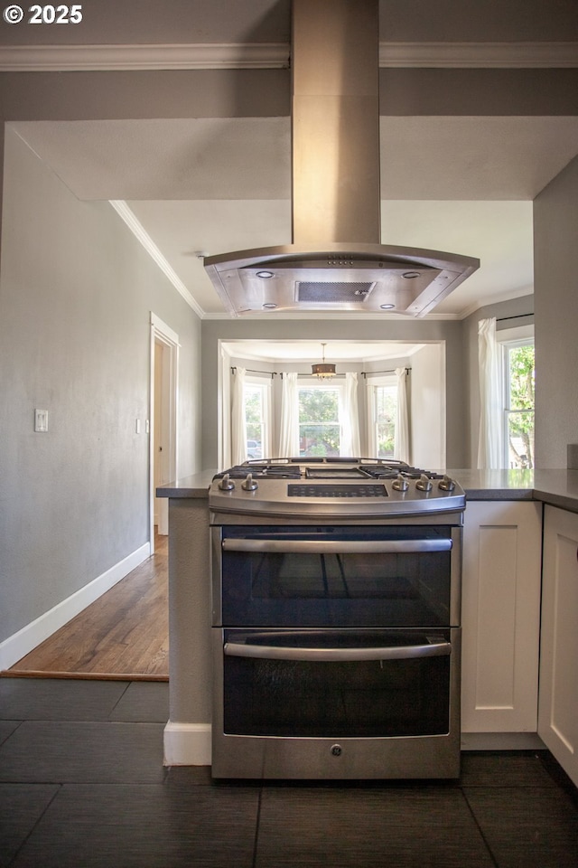 kitchen view of range with two ovens, island exhaust hood, ornamental molding, dark wood-style floors, and white cabinetry