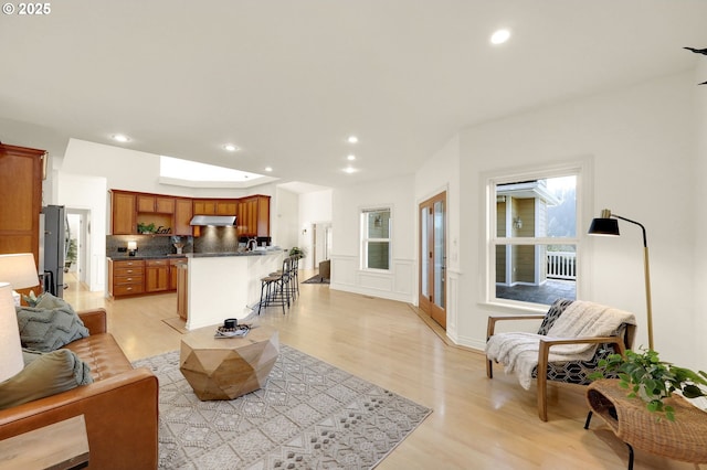 living room featuring a skylight, a wainscoted wall, light wood-type flooring, a decorative wall, and recessed lighting