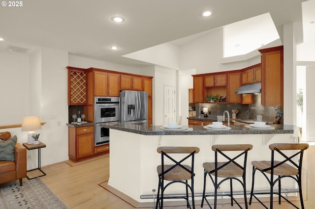 kitchen with a peninsula, appliances with stainless steel finishes, dark countertops, and a breakfast bar