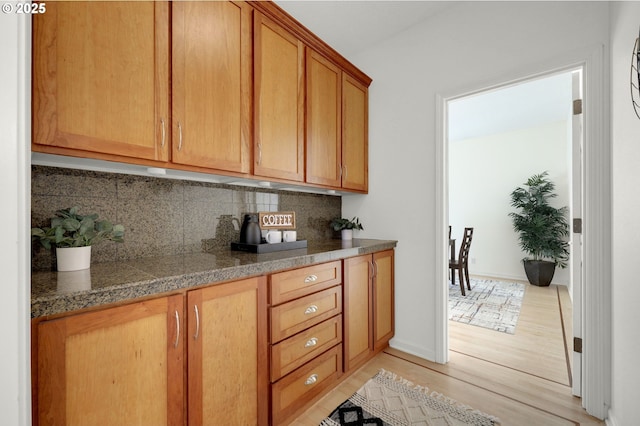 kitchen featuring tasteful backsplash, dark countertops, light wood-style flooring, brown cabinetry, and baseboards