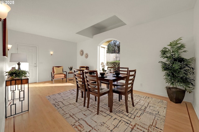 dining area featuring light wood-style floors, arched walkways, and baseboards