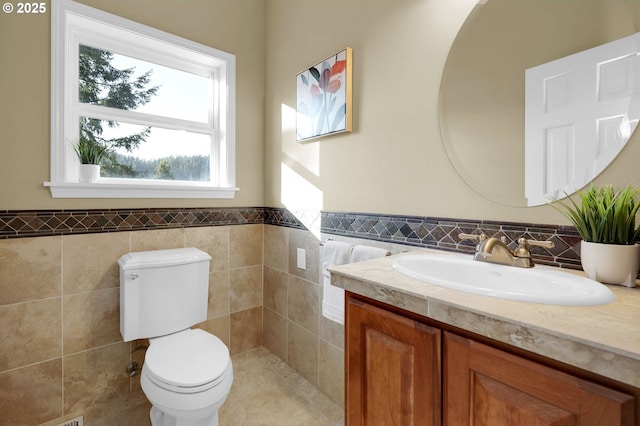 bathroom featuring toilet, wainscoting, vanity, and tile walls