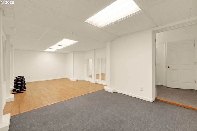 finished basement with wood finished floors, a drop ceiling, carpet flooring, and baseboards