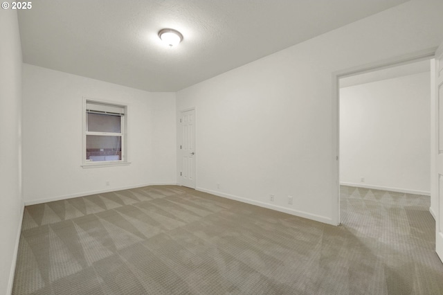 empty room with light carpet, a textured ceiling, and baseboards