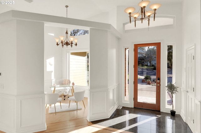 foyer featuring a decorative wall, a wainscoted wall, granite finish floor, a wealth of natural light, and an inviting chandelier