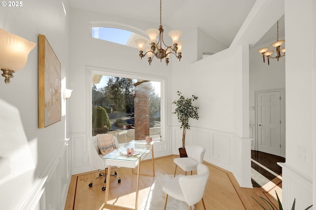 dining room with a decorative wall, a wainscoted wall, a notable chandelier, a high ceiling, and light wood-type flooring