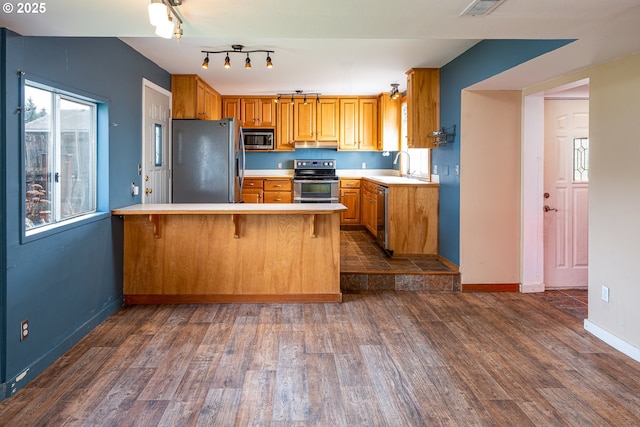 kitchen featuring a sink, dark wood finished floors, appliances with stainless steel finishes, a peninsula, and light countertops