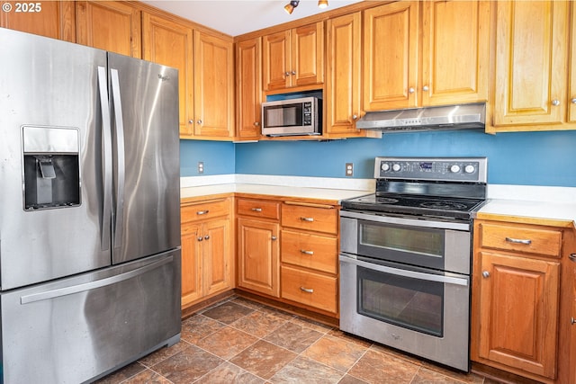 kitchen featuring under cabinet range hood, stainless steel appliances, stone finish floor, and light countertops