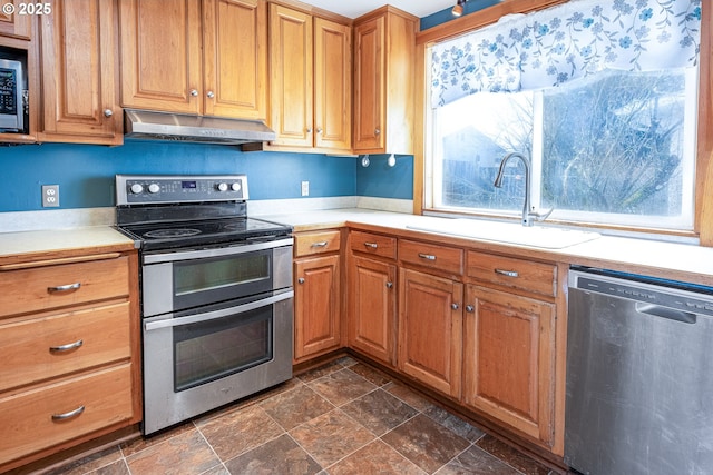 kitchen featuring a sink, light countertops, under cabinet range hood, stone finish flooring, and appliances with stainless steel finishes