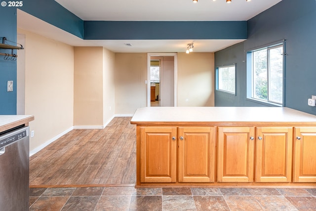 kitchen featuring stone finish flooring, a peninsula, light countertops, baseboards, and dishwasher