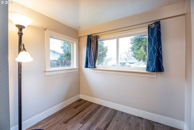 spare room featuring dark wood finished floors, a textured wall, and baseboards