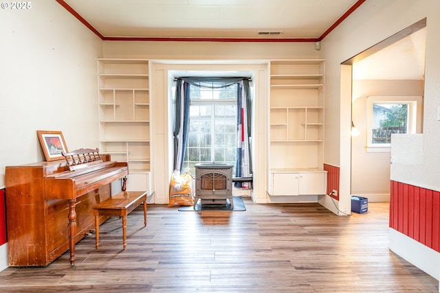 sitting room with visible vents, crown molding, a wood stove, and wood finished floors