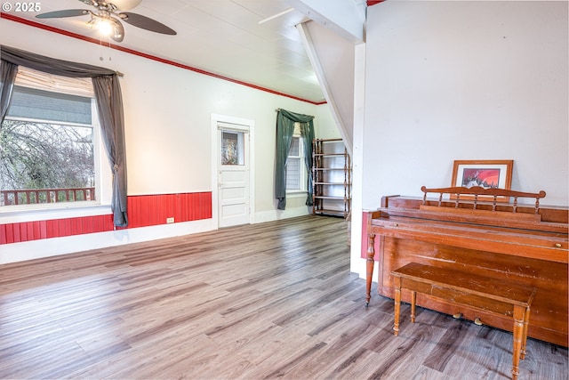 interior space featuring ceiling fan, wood finished floors, wainscoting, and ornamental molding