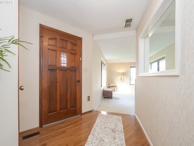 foyer entrance with vaulted ceiling, a textured ceiling, and light hardwood / wood-style flooring