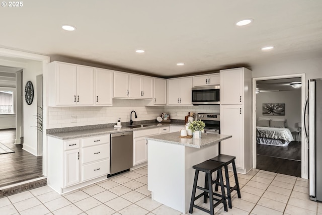 kitchen with light tile patterned flooring, a sink, a kitchen island, white cabinets, and appliances with stainless steel finishes