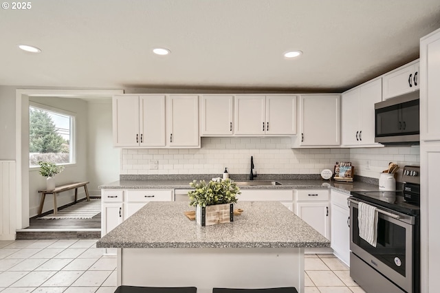 kitchen featuring light tile patterned flooring, a center island, white cabinetry, appliances with stainless steel finishes, and decorative backsplash