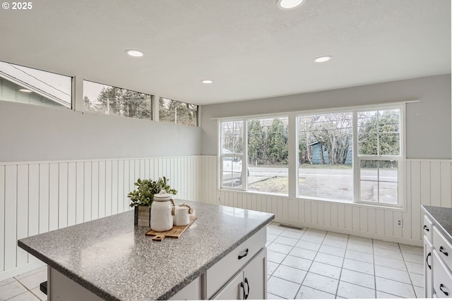 kitchen with a kitchen island, visible vents, white cabinetry, a healthy amount of sunlight, and wainscoting