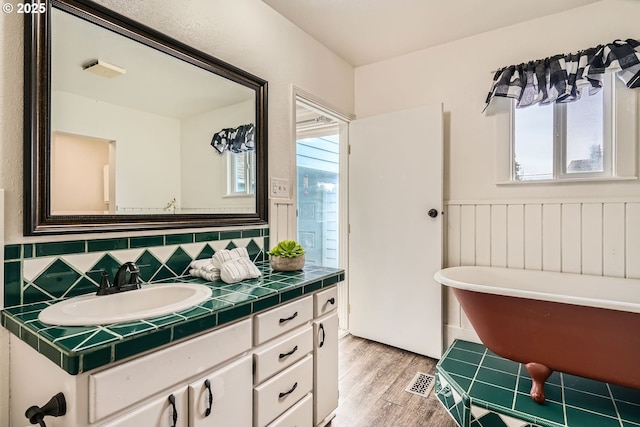 bathroom featuring a wainscoted wall, wood finished floors, vanity, a freestanding bath, and decorative backsplash