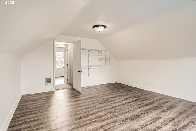 additional living space featuring dark wood-style flooring, visible vents, vaulted ceiling, a textured ceiling, and baseboards