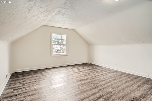 additional living space featuring a textured ceiling, vaulted ceiling, dark wood finished floors, and baseboards