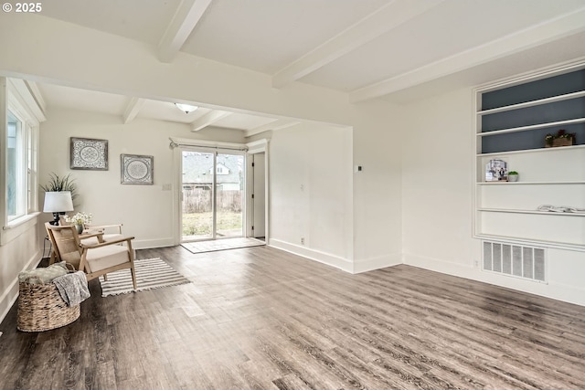 living area featuring baseboards, beam ceiling, visible vents, and wood finished floors