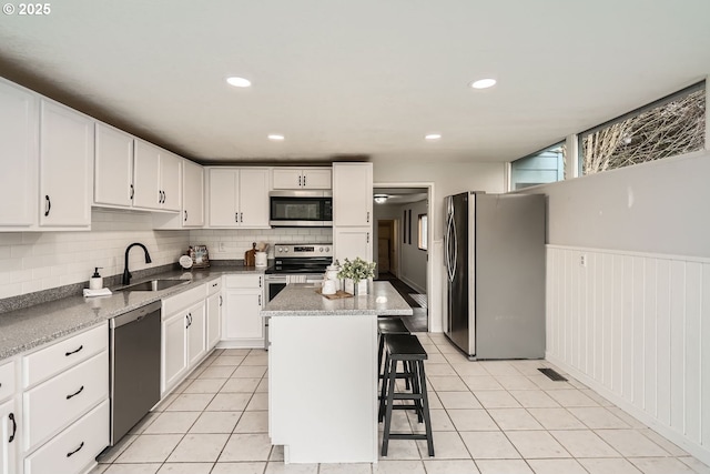 kitchen featuring stainless steel appliances, a sink, white cabinetry, a center island, and a kitchen bar