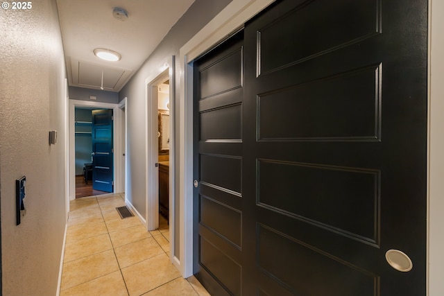 hallway featuring attic access, light tile patterned floors, and baseboards