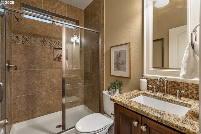 bathroom featuring tasteful backsplash, vanity, toilet, and a shower with shower door