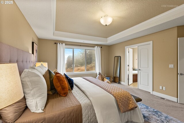 carpeted bedroom featuring a textured ceiling, a tray ceiling, ornamental molding, and ensuite bathroom