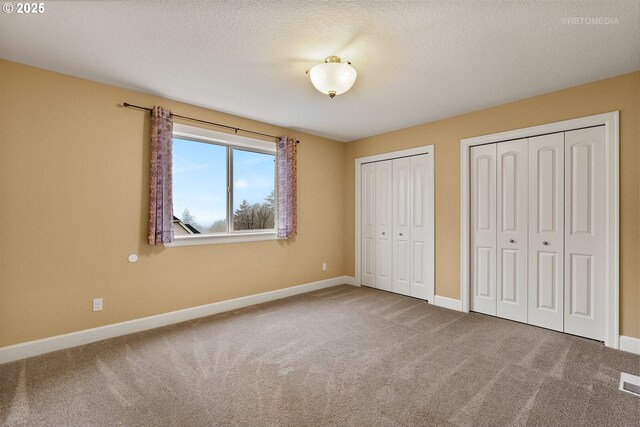 unfurnished bedroom featuring a textured ceiling, carpet flooring, and two closets