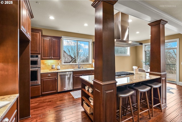 kitchen featuring appliances with stainless steel finishes, a center island, sink, ventilation hood, and decorative columns