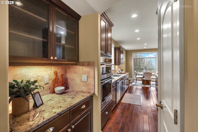 kitchen with island exhaust hood, stainless steel appliances, dark wood-type flooring, light stone countertops, and sink