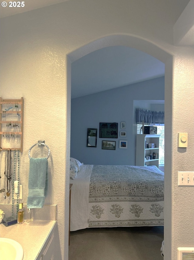 bedroom with a sink, lofted ceiling, a textured wall, and arched walkways