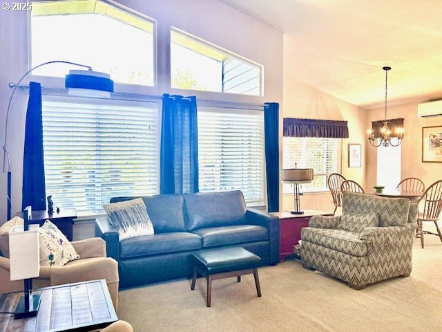 carpeted living room featuring an AC wall unit and a notable chandelier