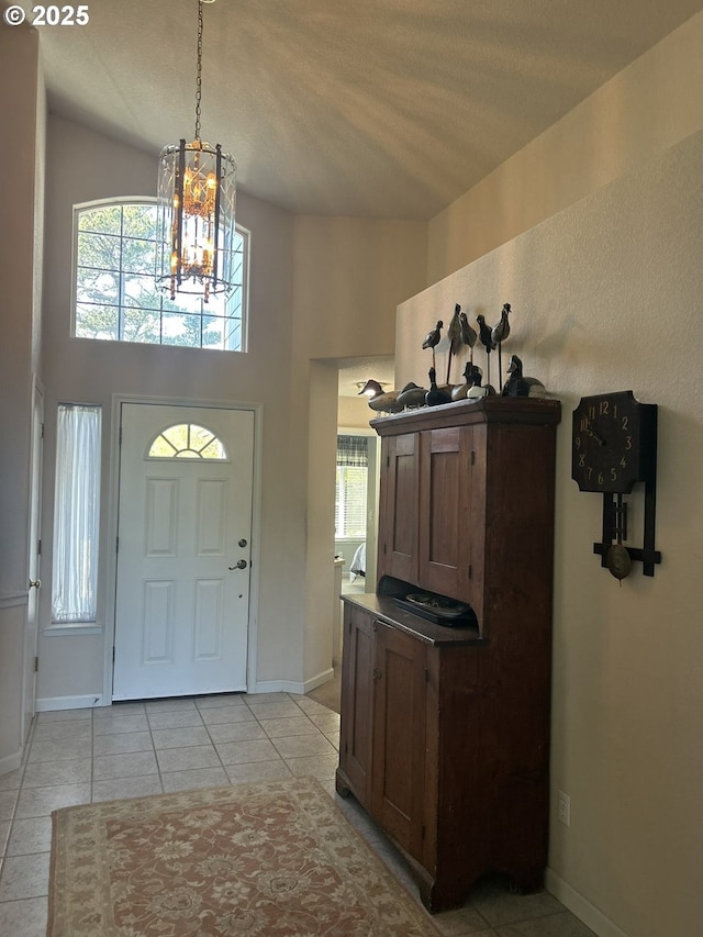 foyer featuring baseboards, a notable chandelier, a healthy amount of sunlight, and a high ceiling